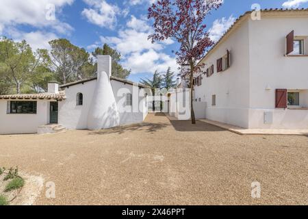 Façades blanches d'une maison de campagne de style cortijo andalou avec des fenêtres avec des volets en bois rouge et des sols en terre cuite et gravier sur un ciel clair jour s. Banque D'Images