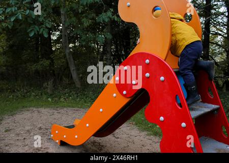 Petit garçon caucasien grimpant sur un toboggan, aire de jeux extérieure Banque D'Images