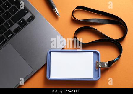 Badge vierge, stylo et ordinateur portable sur fond orange, vue de dessus Banque D'Images