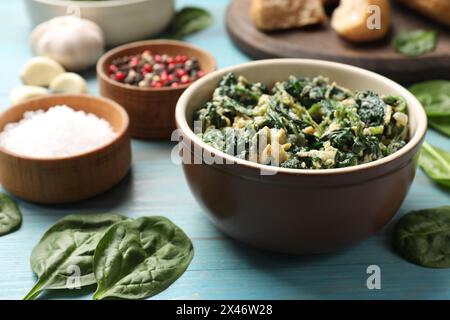 Savoureux trempage aux épinards avec œuf dans un bol et épices sur une table en bois bleu clair, gros plan Banque D'Images