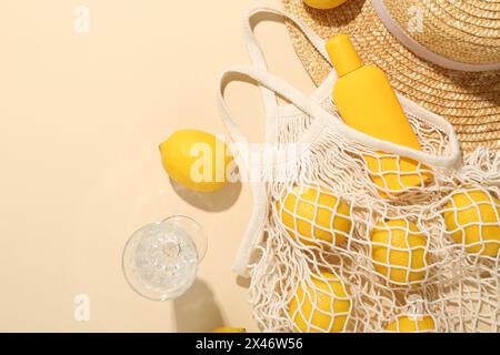 Citrons frais, accessoires de plage dans un sac à ficelle et verre de boisson sur fond beige, pose à plat. Espace pour le texte Banque D'Images