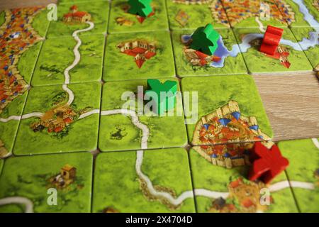 Mozyr, Biélorussie, 03 avril 2024 : jeu de société carcassonne rouge vert meeple se trouvent sur la carte de terrain règles de jeu pour occuper le terrain. Banque D'Images