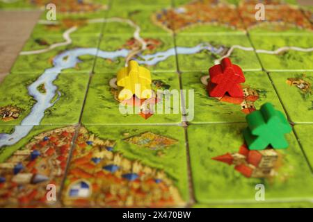 Mozyr, Biélorussie, 03 avril 2024 : jeu de société familial carcassonne vert jaune rouge meeple sur les tuiles de la carte du terrain de jeu. Règles pour placer Monaster Banque D'Images
