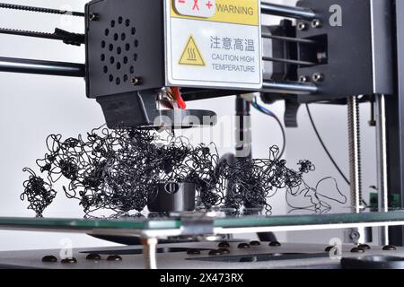 Echec de l'imprimante 3D. Filament plactique extrudé aléatoirement. PLA noir gondolé non collé à la partie imprimée. Banque D'Images