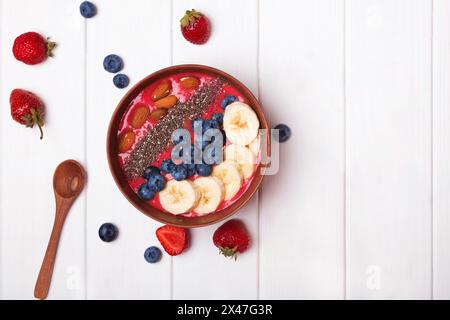 Bol à smoothie aux fraises surmonté de baies et de bananes sur la table blanche. Petit déjeuner sain, vue de dessus Banque D'Images