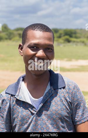 village célibataire jeune homme africain avec un sourire dentelé, à l'extérieur dans la nature dans un champ vert Banque D'Images