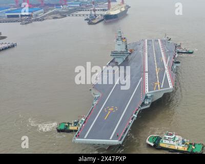 (240501) -- SHANGHAI, 1er mai 2024 (Xinhua) -- une photo de drone aérien prise le 1er mai 2024 montre des remorqueurs remorquant le troisième porte-avions chinois, le Fujian, loin d'un quai dans l'est de la Chine Shanghai. Le troisième porte-avions de la Chine, le Fujian, s'est lancé mercredi matin pour ses premiers essais en mer. Les essais en mer porteront principalement sur la fiabilité et la stabilité des systèmes de propulsion et électriques du porte-avions. Depuis son lancement en juin 2022, le Fujian a terminé ses essais d'amarrage, ses travaux d'équipement et ses ajustements d'équipement. Il a satisfait aux exigences techniques pour les essais en mer. ( Banque D'Images