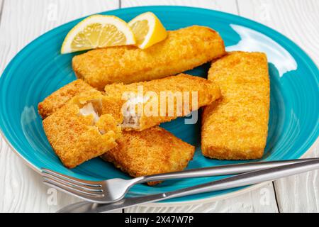 filet de pollock d'alaska pané croustillant avec couverts et tranches de citron sur plat bleu sur table en bois blanc, vue paysage, gros plan Banque D'Images