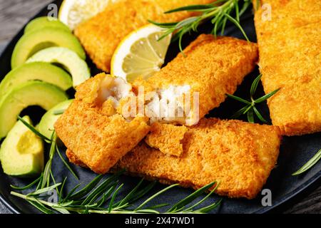 filet de pollock d'alaska croustillant cuit au four sur plat noir avec des tranches de romarin, de citron et d'avocat sur une table en bois rustique, gros plan Banque D'Images