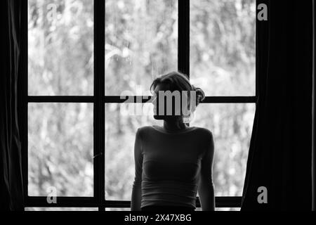 Jeune femme regardant par une fenêtre en Monochrome Banque D'Images
