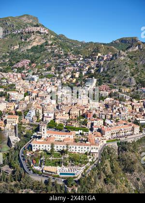 VUE AÉRIENNE. La ville touristique de Taormina, et ci-dessus sur la gauche, le village perché de Castelmola. Ville métropolitaine de Mesina, Sicile, Italie. Banque D'Images