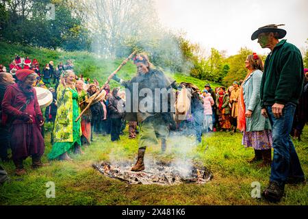 Les gens sautent le feu pendant les célébrations de Beltane à Glastonbury Chalice Well, où ils observent une interprétation moderne de l'ancien rite de fertilité païenne celtique du printemps. Date de la photo : mercredi 1er mai 2024. Banque D'Images