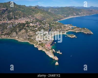 VUE AÉRIENNE. Les promontoires rocheux de Taormina se projetant dans la mer Ionienne. Ville métropolitaine de Messine, Sicile, Italie. Banque D'Images