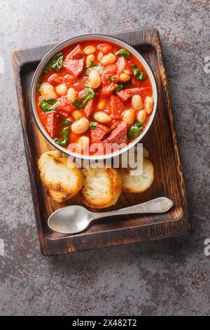 Chorizo, haricots rouges et épinards gros plan dans un bol servi avec du pain grillé sur la table. Vue de dessus verticale Banque D'Images