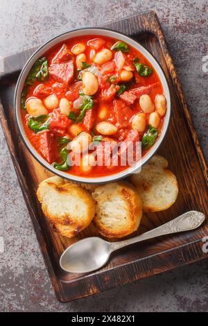 Ragoût cuit lentement de haricots, chorizo et épinards dans une sauce tomate gros plan dans un bol sur la table. Vue de dessus verticale Banque D'Images