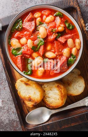 Ragoût de haricots copieux avec saucisses, épinards et épices dans une sauce tomate gros plan dans un bol servi avec du pain grillé sur la table. Vue de dessus verticale de Banque D'Images