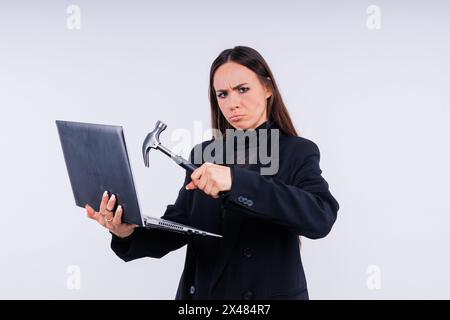 Femme attrayante portant un costume d'affaires avec une expression faciale en colère par ordinateur tenant un marteau Banque D'Images