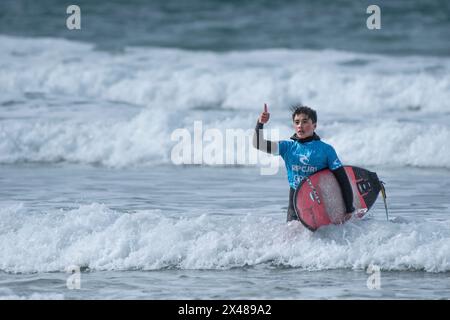 Un jeune surfeur masculin portant sa planche de surf et donnant un pouce vers le haut et marchant hors de la mer après avoir participé au concours de surf Rip Curl Grom Search Banque D'Images