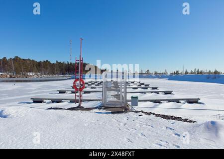 Port de plaisance vide avec des quais enneigés et sol avec de la glace de mer gelée par une froide journée d'hiver par temps ensoleillé, Loviisa, Finlande. Banque D'Images