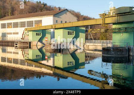 Centrale hydroélectrique. Réflexion des maisons et des équipements dans l'eau douce. Colline avec des arbres en arrière-plan. Ciel bleu. Banque D'Images