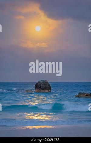 Lune rose se levant et se reflétant dans l'eau avec des vagues se brisant doucement Bermudes Banque D'Images