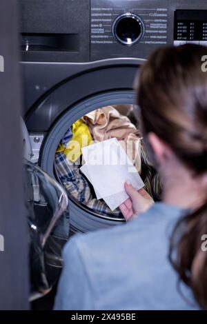 Femme assis devant une machine à laver chargeant des vêtements sales, serviettes pour laver des vêtements colorés. Banque D'Images