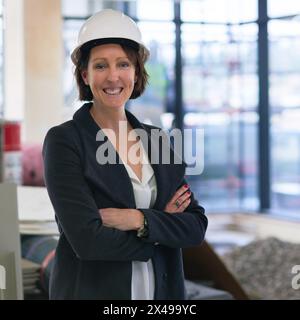 Sourire, portrait et femme dans le chantier pour la construction, action positive et visite d'inspecteur dans le bâtiment. Entrepreneur, employé féminin et inspection de Banque D'Images