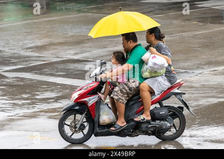 SAMUT PRAKAN, THAÏLANDE, 20 mars 2024, Une famille avec des parapluies qui fait du vélo sous la pluie Banque D'Images