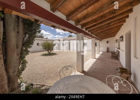 Porche couvert avec toit en bois d'une maison de campagne de style ferme andalouse avec trottoirs en terre cuite et allée de gravier. Banque D'Images