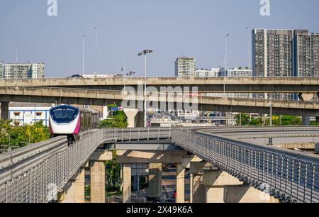 Vue urbaine voies ferrées banlieues monorail trains électriques de banlieue se précipitant sur le pont supérieur soutient les bâtiments, les voitures et les camions conduisent une autoroute à trafic dense Banque D'Images