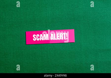 Mots d'alerte d'arnaque écrits sur un autocollant de papier rose avec fond vert. Symbole d'alerte d'arnaque conceptuelle. Copier l'espace. Banque D'Images