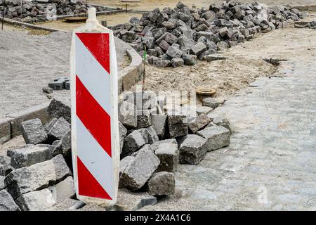 Pavage de rues avec pavés historiques en granit martelé, restauration de la surface des rues de la ville, cubes de roches, signalisation verticale rayée rouge et blanche Banque D'Images