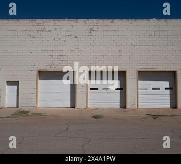 négligé et daté mais fonctionnel délabrement urbain commercial avec l'ambiance du milieu du siècle, trois portes de garage blanches dans un bâtiment en briques blanches avec porte Banque D'Images