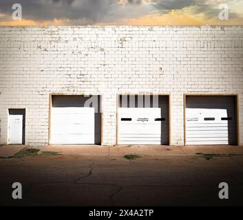 négligé et daté mais fonctionnel délabrement urbain commercial avec l'ambiance du milieu du siècle, trois portes de garage blanches dans un bâtiment en briques blanches avec porte Banque D'Images