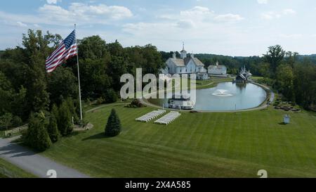 Vue aérienne d'Un grand bâtiment blanc avec Un toit gris entouré de pelouses vertes luxuriantes, Un grand étang réfléchissant avec des fontaines et Un mât de drapeau majestueux Banque D'Images