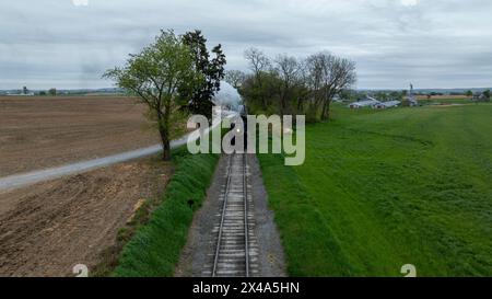 Un train descend une voie à côté d'un champ. Le train est noir et de la vapeur sort de l'avant Banque D'Images