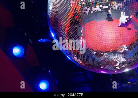 Grande boule disco classique faite de petits miroirs reflétant des lumières vives et chaudes sur le plafond d'une discothèque ou d'une salle de concert. La piste de danse peut l'être Banque D'Images