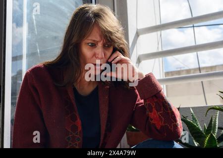 femme adulte assise sur le balcon de l'appartement est indignée parlant au téléphone très en colère Banque D'Images