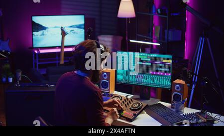 Ingénieur du son synchronisant les pistes vidéo et audio dans son home studio, montage des techniques sur les enregistrements. Jeune artiste ajustant le volume de la musique après avoir mixé et masterisé des morceaux avec l'amplificateur. Caméra B. Banque D'Images