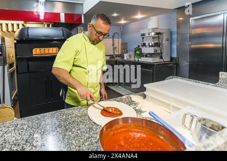 chef ajoutant de la sauce tomate fraîche à la pâte à pizza. Ingrédients de pizza. Photo de haute qualité Banque D'Images