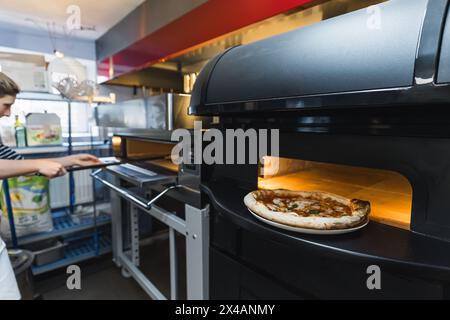 femme cuisinier préparant des pizzas dans la cuisine, four électrique, boulangerie. Photo de haute qualité Banque D'Images