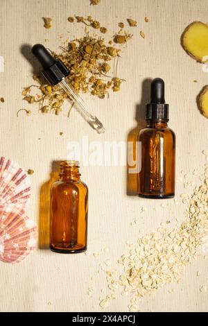 Une bouteille d'huile essentielle posée sur des rochers sur une table en bois naturel avec un dahlia rose sur le côté. Banque D'Images
