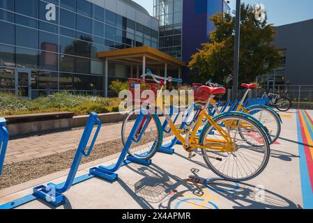 Vélo jaune vif avec panier rouge garé dans le porte-vélos bleu au bâtiment moderne. Banque D'Images