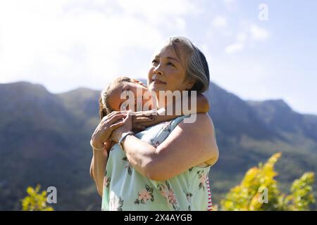 Grand-mère asiatique et petite-fille adolescente biraciale embrassant à l'extérieur. Grand-mère aux cheveux gris et petite-fille aux cheveux blonds partageant une maman paisible Banque D'Images