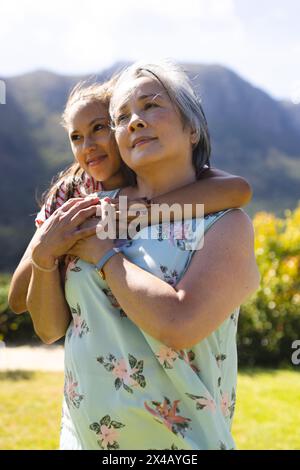 Grand-mère asiatique et petite-fille adolescente biraciale embrassant à l'extérieur. Les deux arborent les cheveux foncés, jeune femme montrant un sourire chaleureux, partageant un moment joyeux Banque D'Images