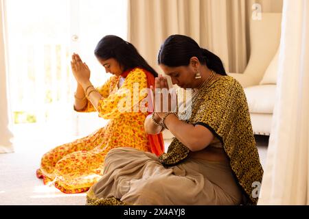 Mère indienne et fille adolescente, portant des vêtements traditionnels, priant ensemble à la maison. Tous deux avec de longs cheveux noirs, partageant un moment calme dans un cadre serein Banque D'Images
