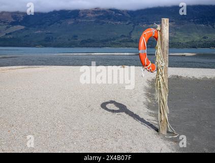 Bouée de sauvetage orange suspendue à un poteau en bois sur une plage près d'un lac. Beau paysage Banque D'Images