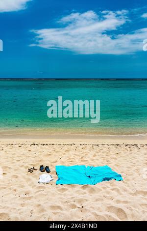 Tongs et serviette de plage bleue sur le sable près de la mer Banque D'Images