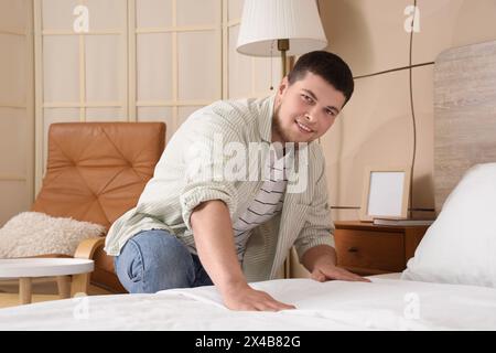 Jeune homme barbu faisant le lit dans la chambre Banque D'Images