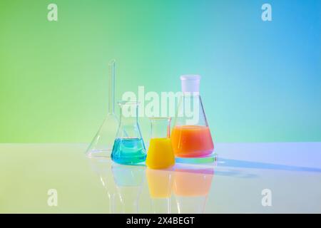 Vue avant des équipements de laboratoire - différentes tailles de flacons erlenmeyer remplis de liquide de couleur, sur fond dégradé vert et bleu. Concept : recherche Banque D'Images